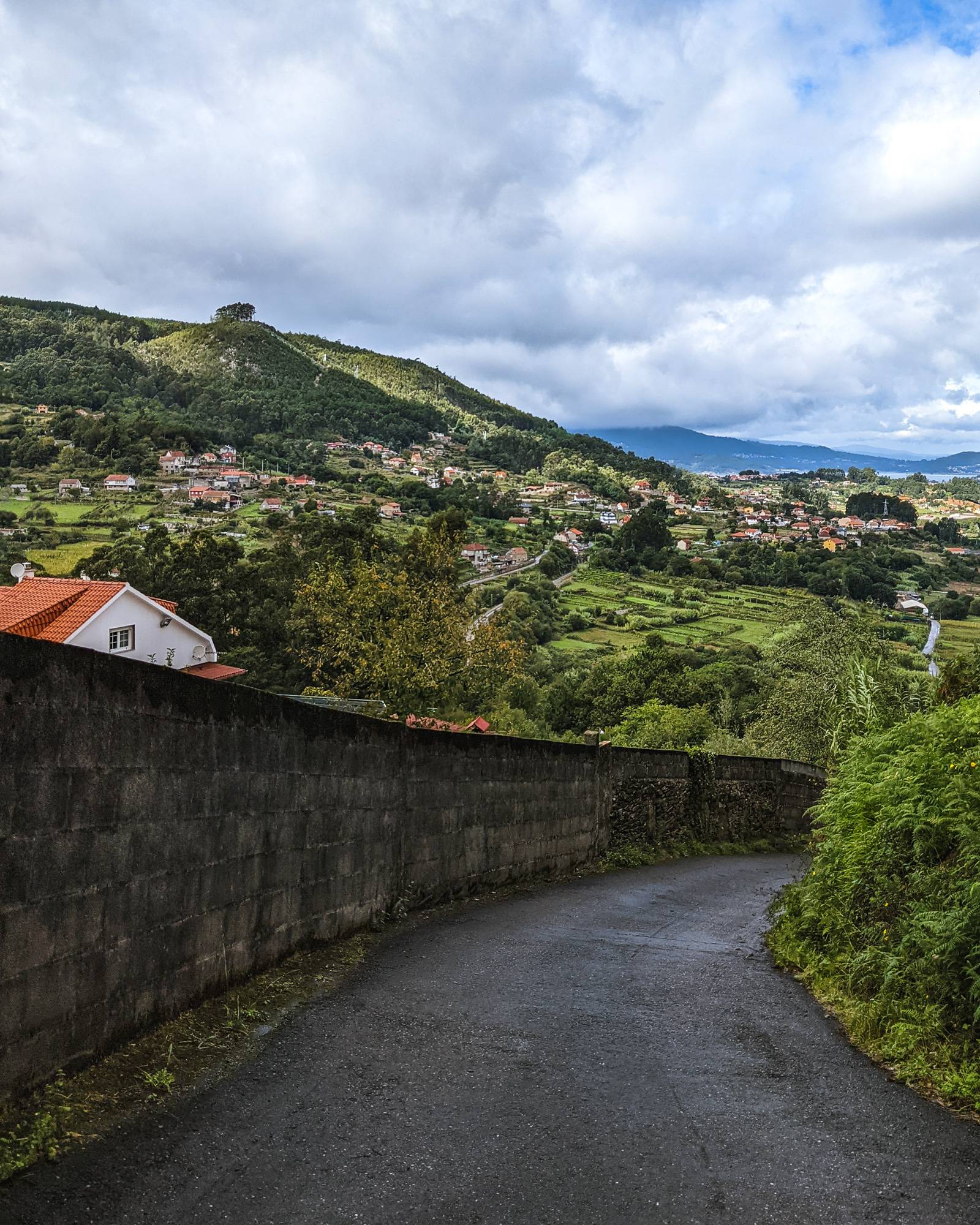 Downhill road on the Portuguese Camino central route with the green hills of Spain in the background