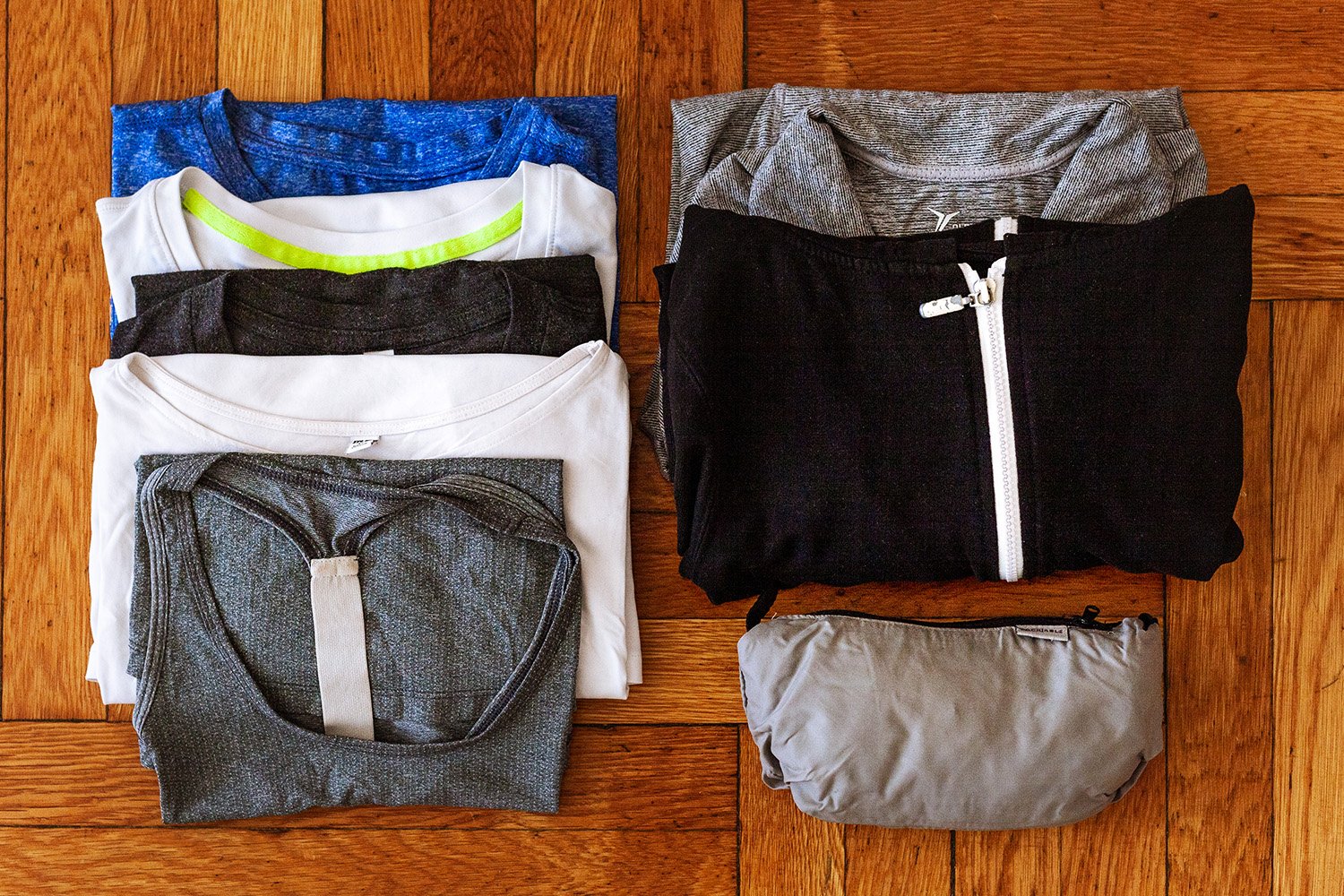 Four t-shirts, one tank top, two zip-up jackets, and a packable rain jacket flat lay on a wooden floor