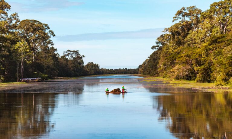 Two workers on a raft in the middle of the river outside of Bayon Temple in Angkor Wat