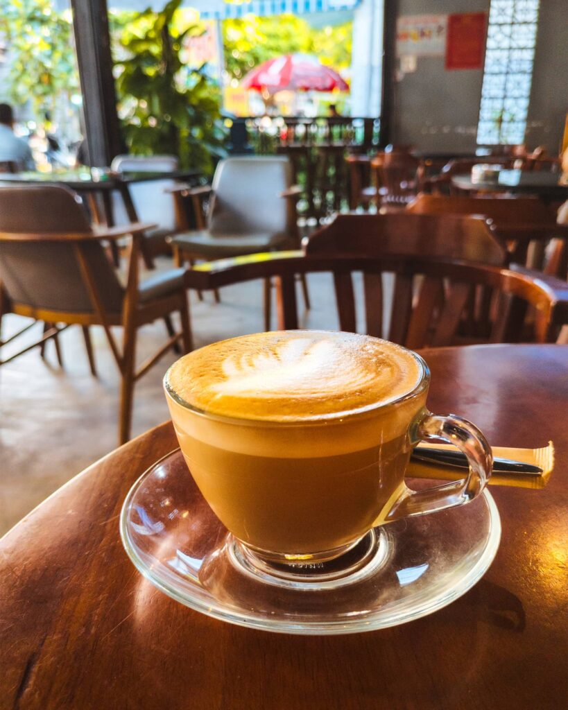 Latte in a clear cup on a wood table at Bean House Coffee in Nha Trang