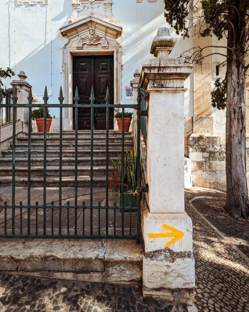 Front of the Church of Saint James in Lisbon with an iron gate and a yellow Camino de Santiago arrow