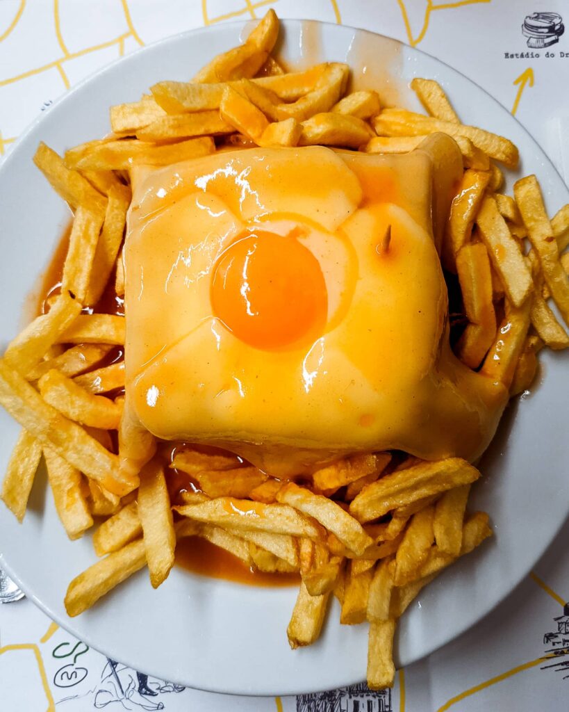 Top down view of a francesinha sandwich, with an egg on top and fries surrounding it, at Cafe Santiago