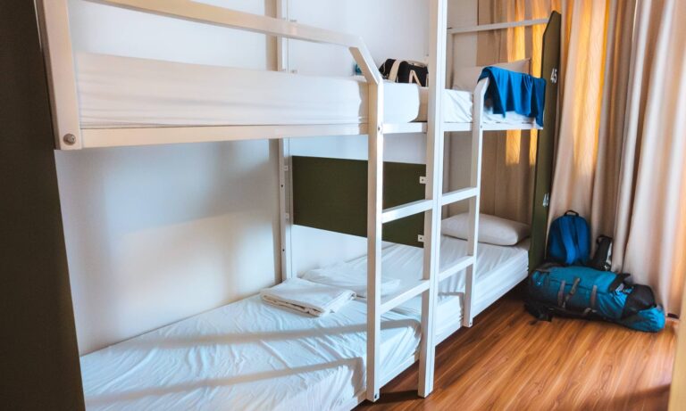A blue towel draped over a bunk bed railing and two blue backpacks next to a bunk bed in a hostel dorm room